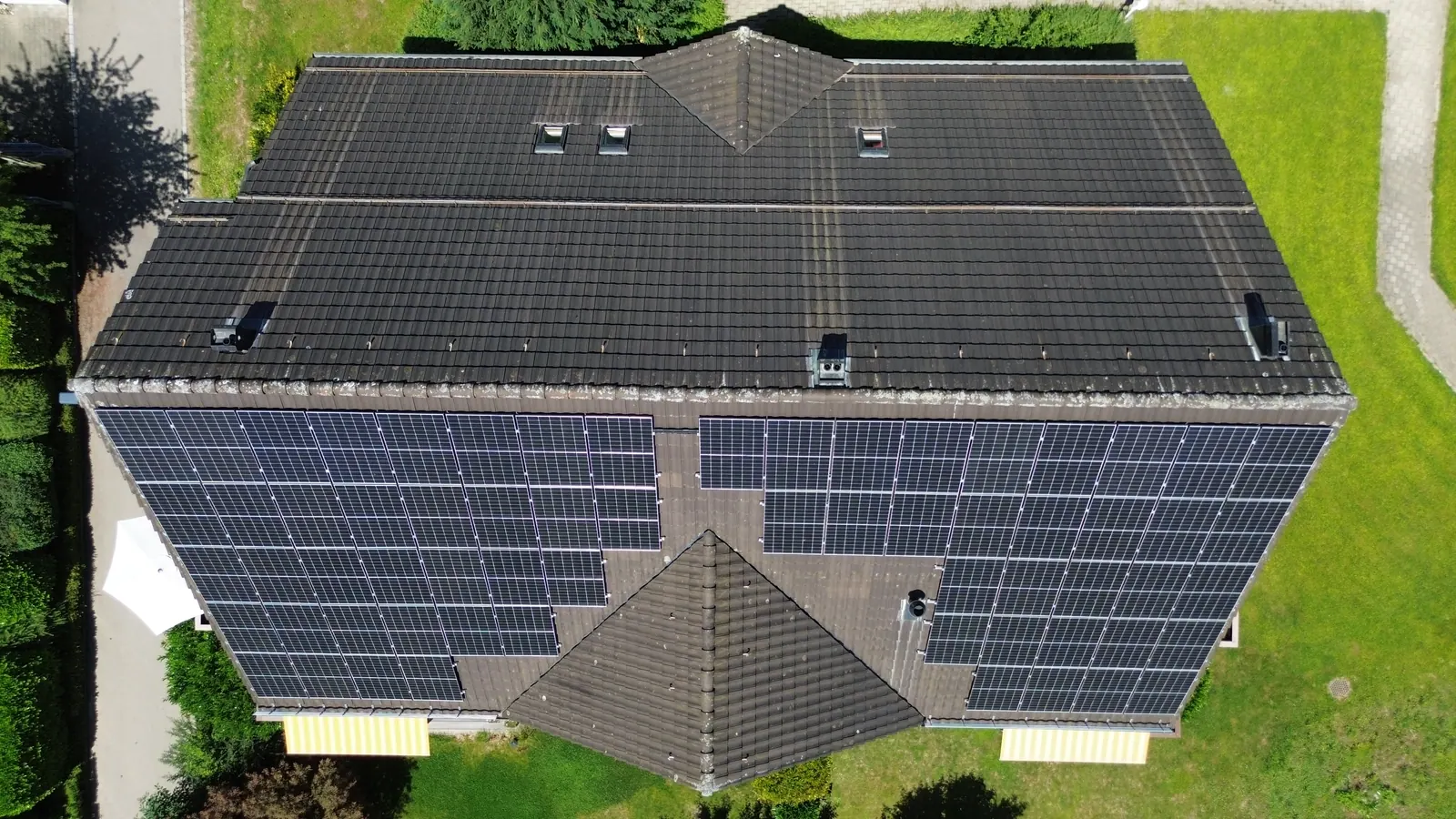 Drohnenaufnahme von oben: Schrägdach eines Mehrfamilienhauses, vollflächig mit Solarmodulen belegt