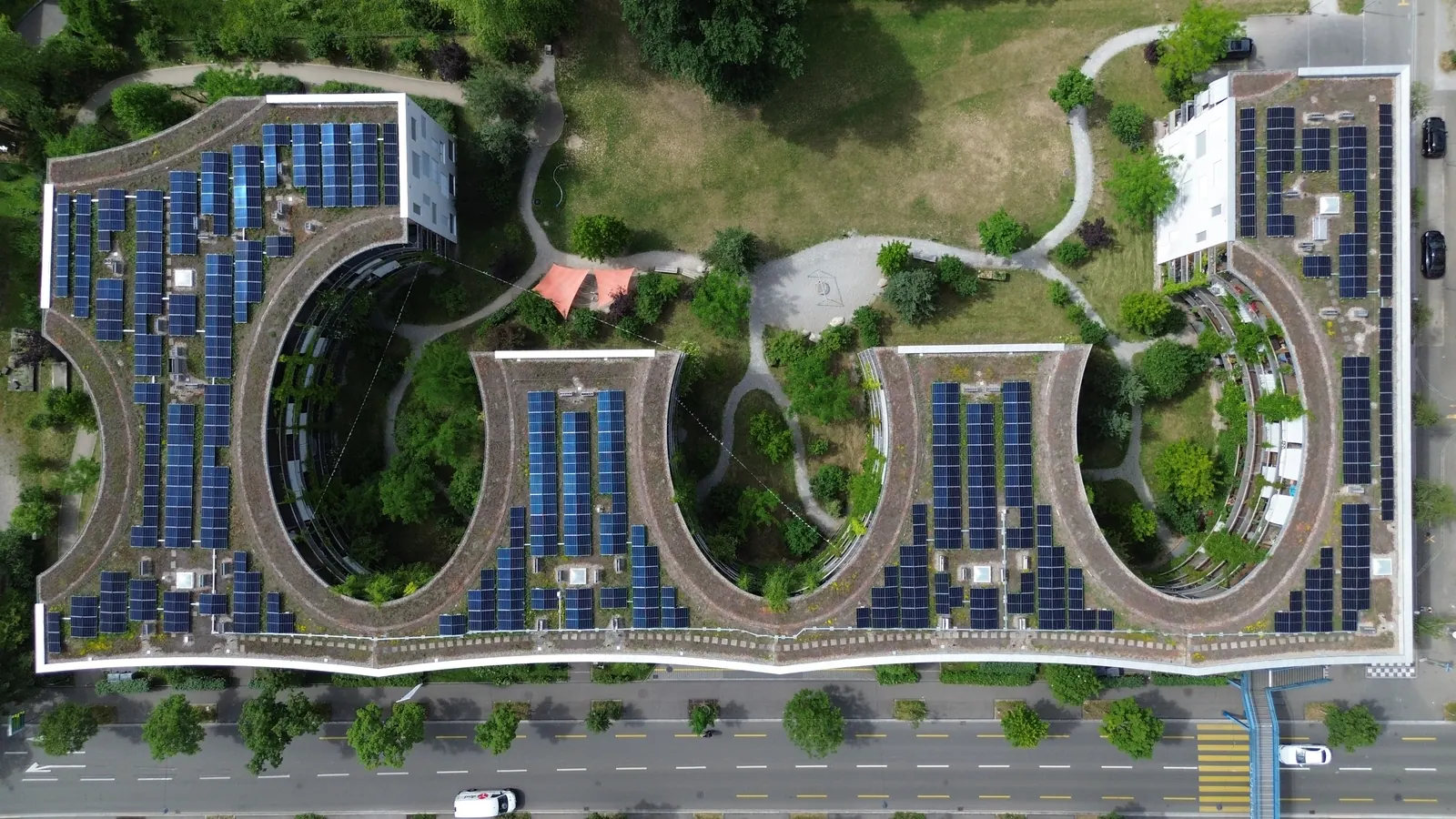 Drohnenaufnahme von oben: geschwungene Dächer einer Siedlung, vollständig mit Solarmodulen belegt